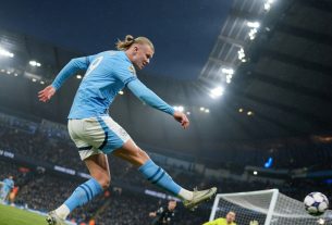 Erling Haaland, in a sky-blue kit without logos, captured from a low angle as
