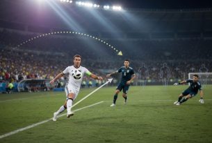 Low sideline sports photo at night of Mario Götze chesting the ball and beginning