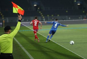 Assistant referee flags offside as a red-clad striker stands past the last blue defender;
