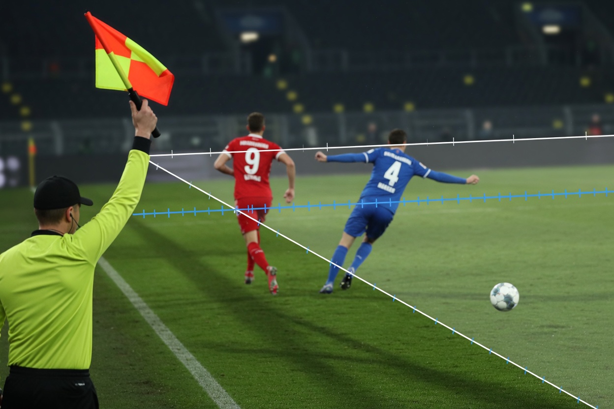 Assistant referee flags offside as a red-clad striker stands past the last blue defender;