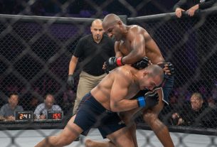Fotografische Szene in einem neutralen MMA-Oktagon: zwei anonyme Profikämpfer, einer verteidigt per Sprawl gegen